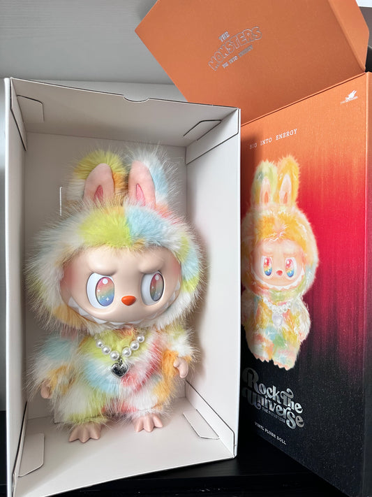 Colorful plush toy with a pearl necklace in an open box, with a blurred background.