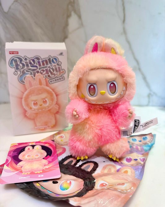 Pink plush toy with bunny ears and a box labeled 'Big Into Small' on a white surface.