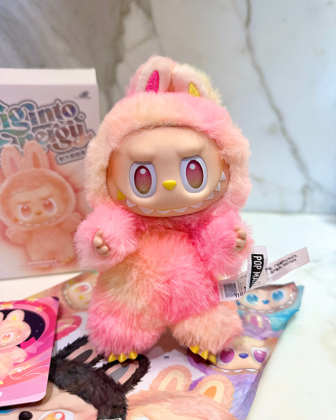Pink plush toy with a fluffy hood on a white surface