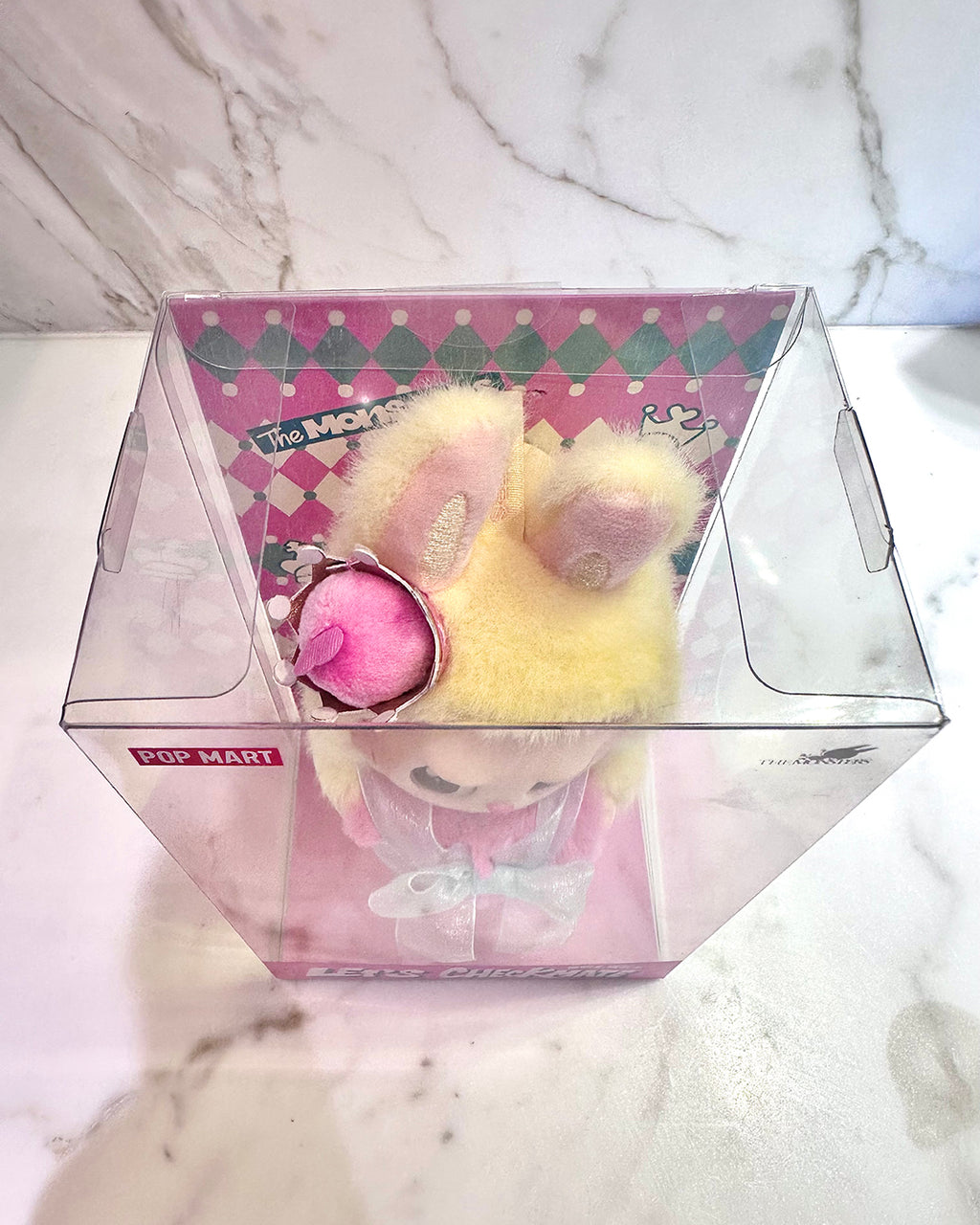 Small plush toy in a clear box on a marble surface