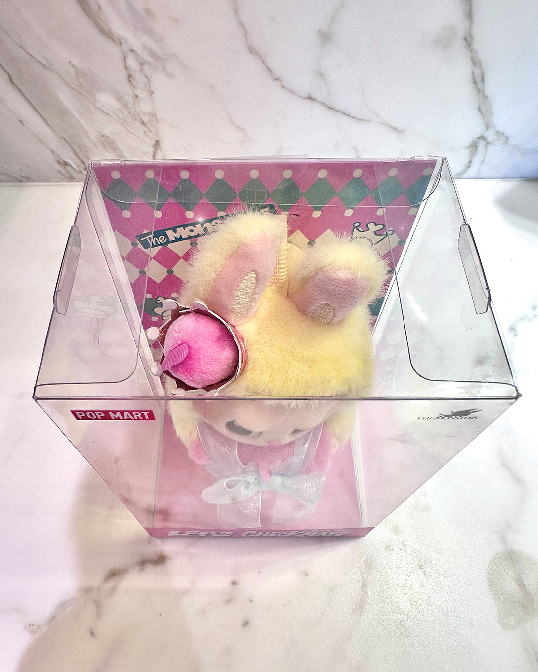 Small plush toy in a clear box on a marble surface