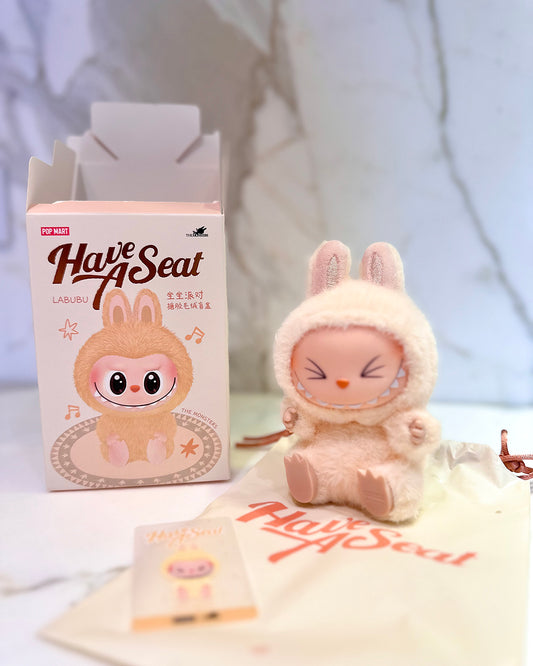 Plush toy and packaging with 'Have A Seat' branding on a light background