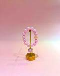 Pink beaded bracelet on a gold stand against a gradient pink background