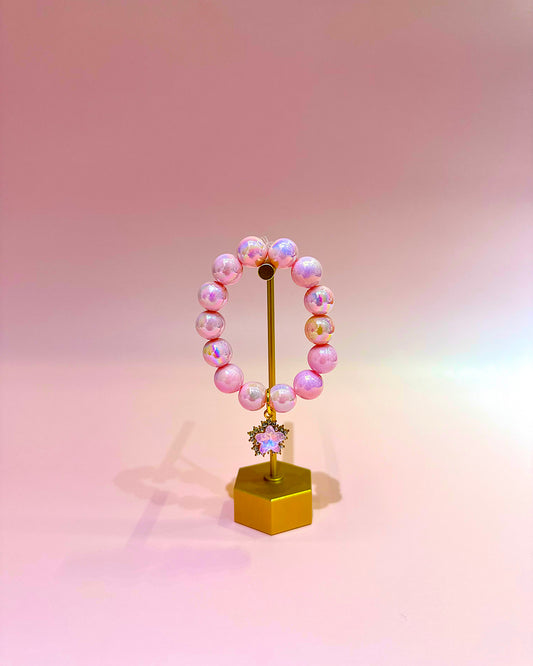 Pink beaded bracelet on a gold stand against a gradient pink background