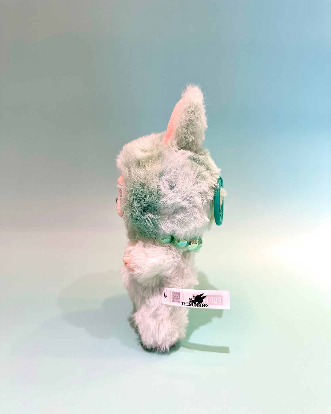 Plush toy resembling a unicorn with a green horn and mane on a light blue background
