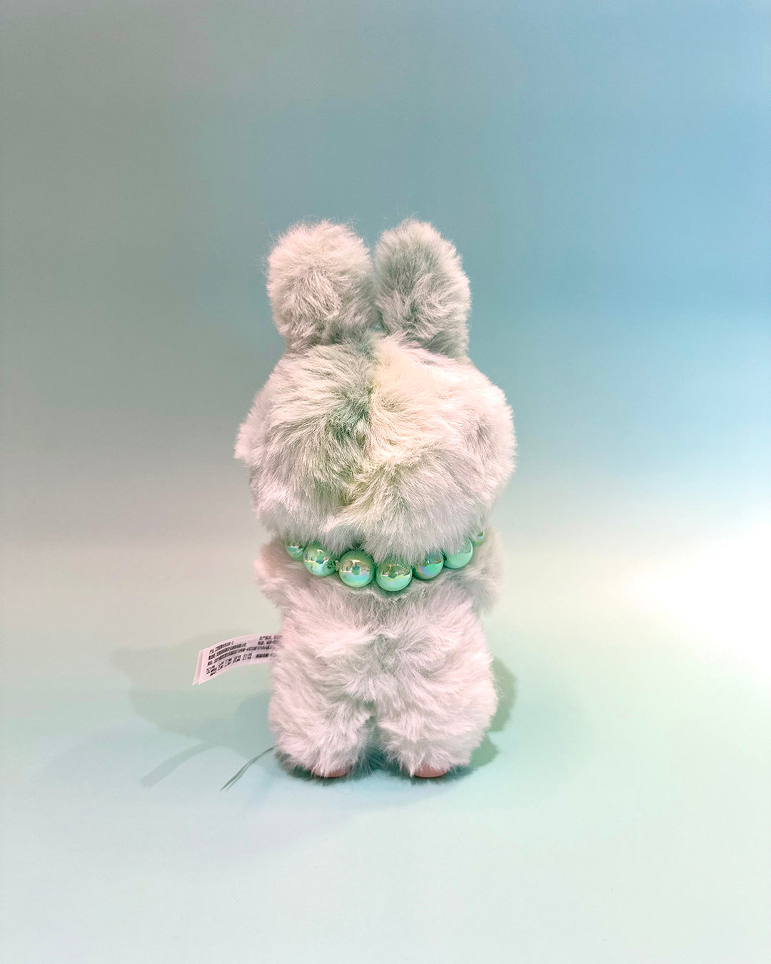 White plush toy with pom-poms on a gradient background