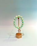 Green beaded bracelet on a gold stand with a white background