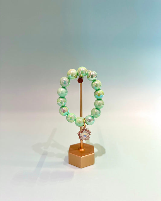 Green beaded bracelet on a gold stand with a white background