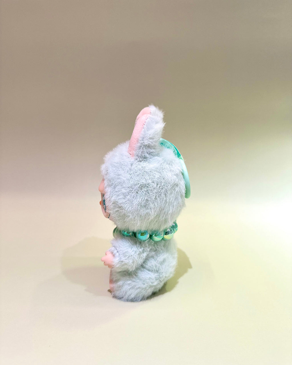 Small plush toy with a fluffy white head and green body on a beige background