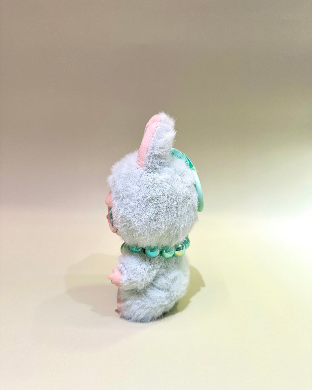 Small plush toy with a fluffy white head and green body on a beige background