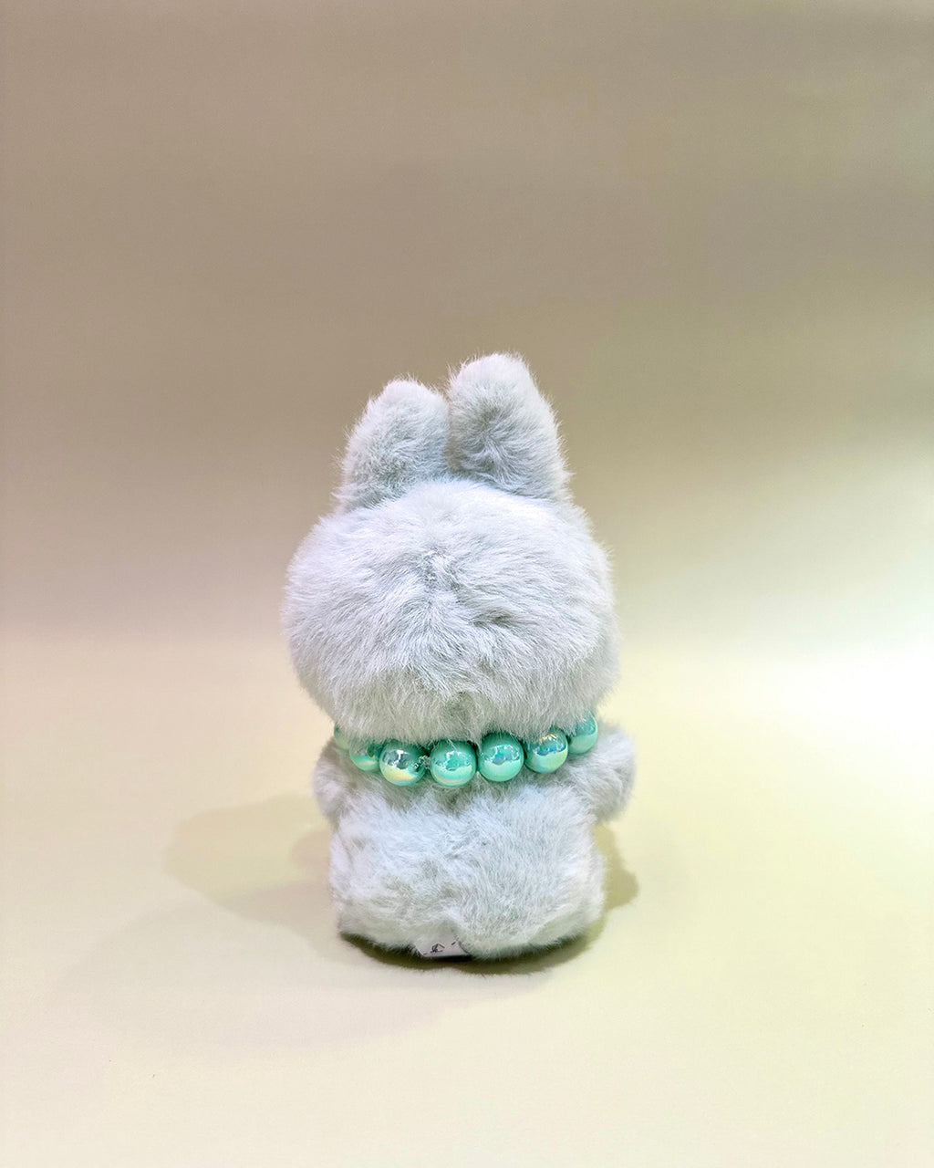 Plush toy with a green beaded necklace on a beige background