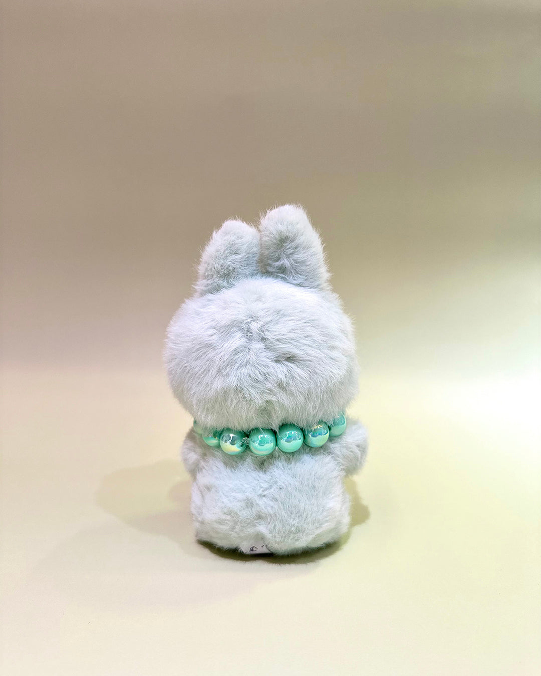 Plush toy with a green beaded necklace on a beige background