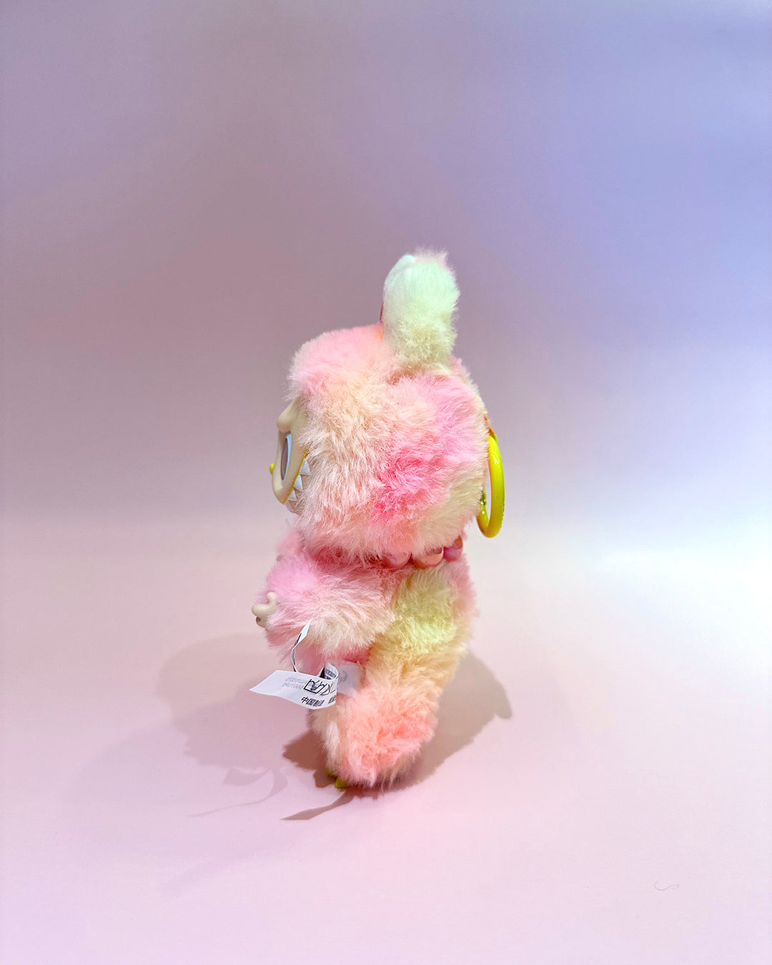 Pastel-colored plush toy with a tag on a gradient background