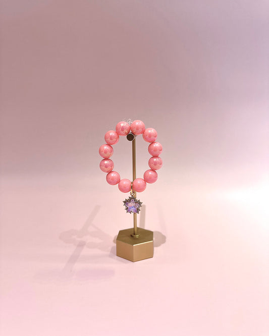 Pink beaded bracelet on a stand with a hexagonal base against a pink background