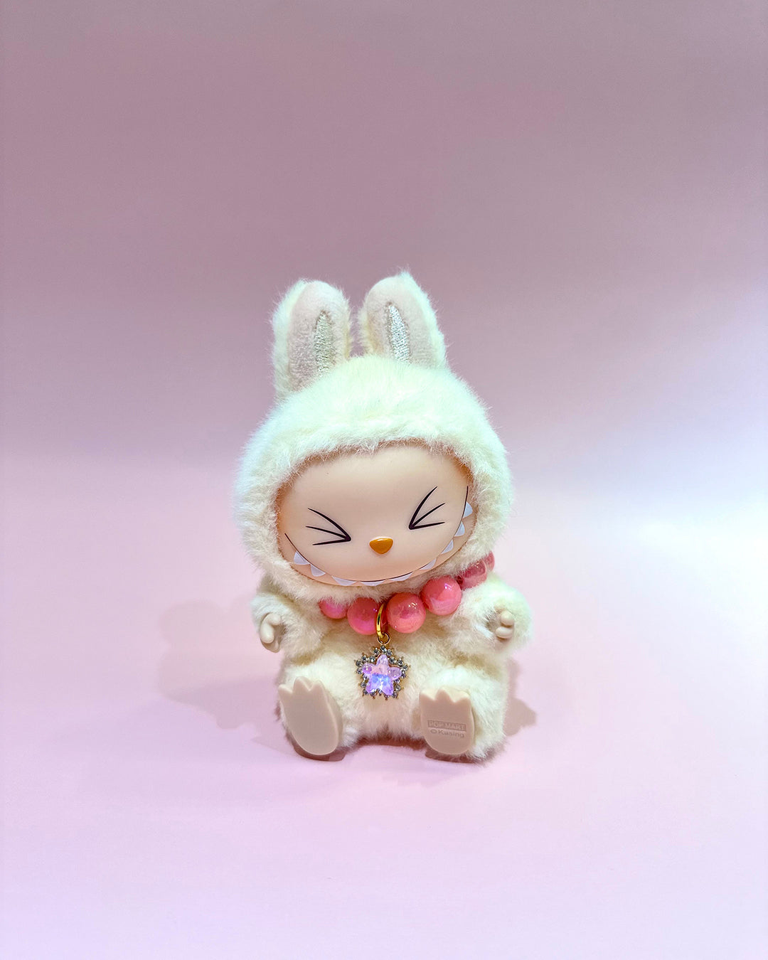 White plush toy with bunny ears and pink beads on a light pink background