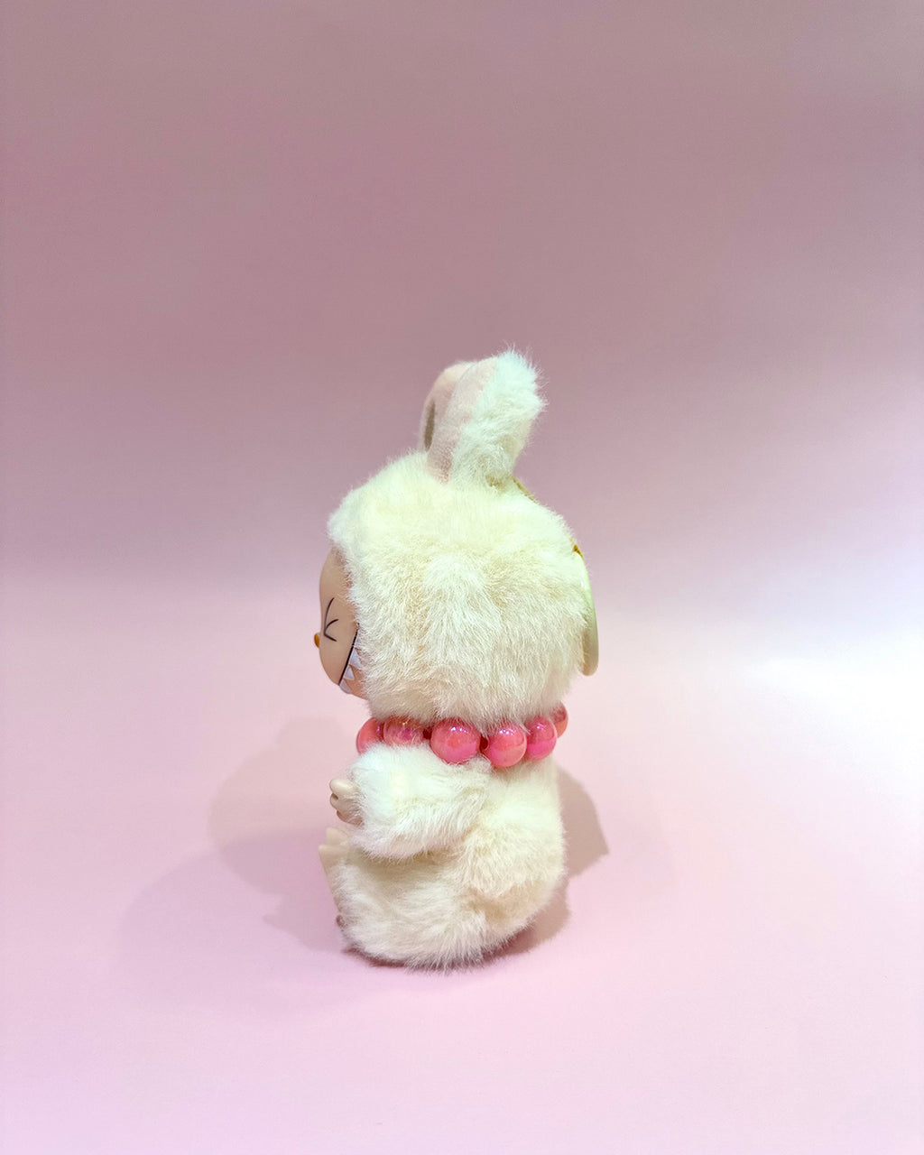 Small plush toy with a pink bow on a pink background