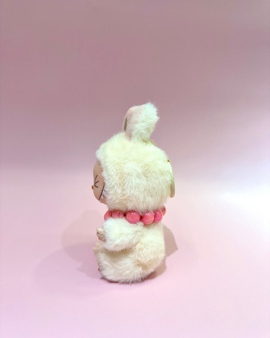 Small plush toy with a pink bow on a pink background