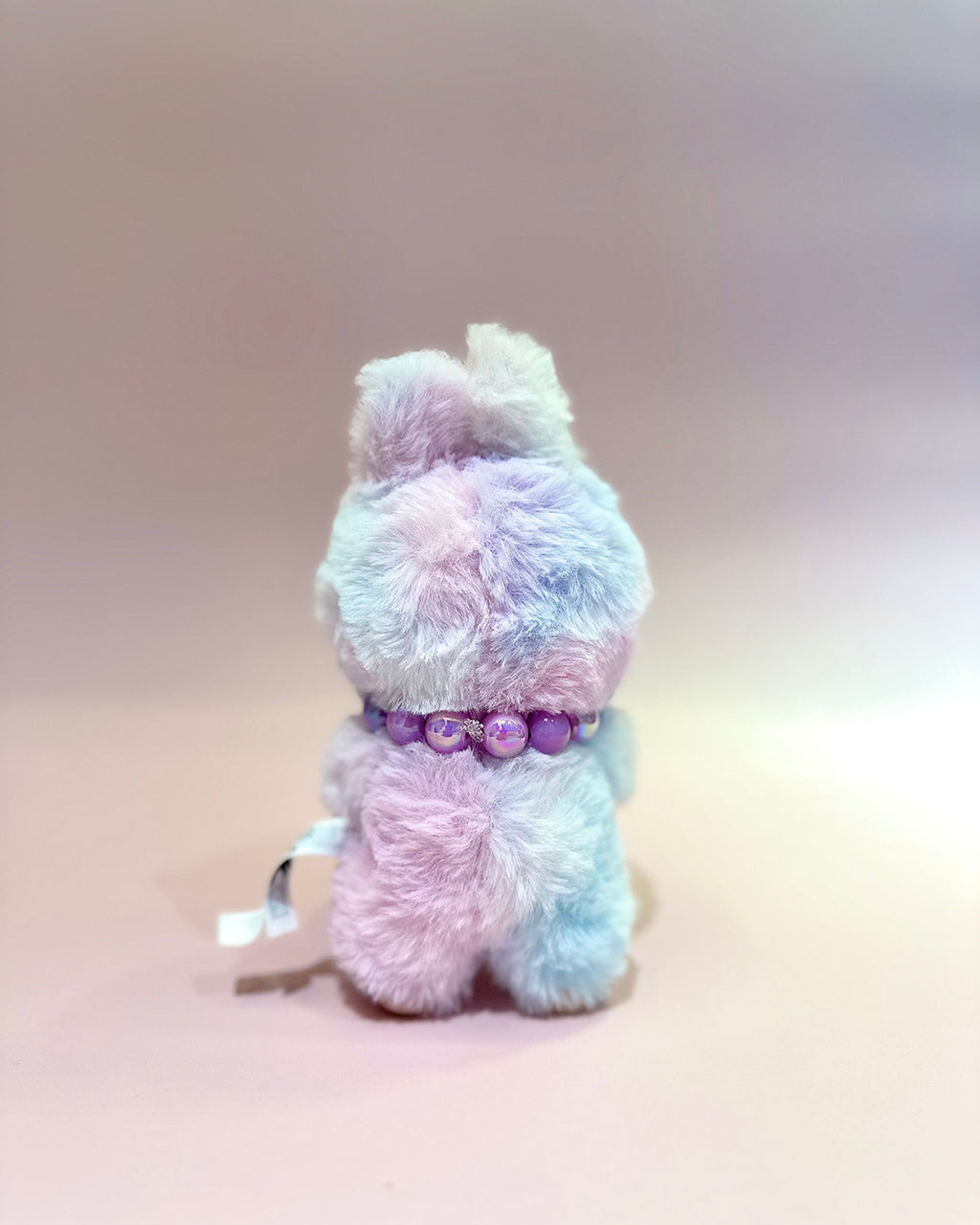 Pastel-colored plush toy with a purple collar on a gradient background