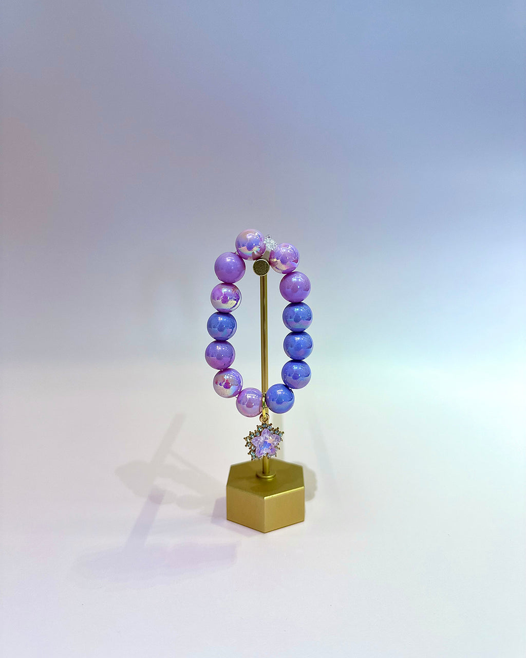 Purple beaded bracelet on a gold stand with a white background