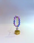 Purple beaded bracelet on a gold stand with a white background