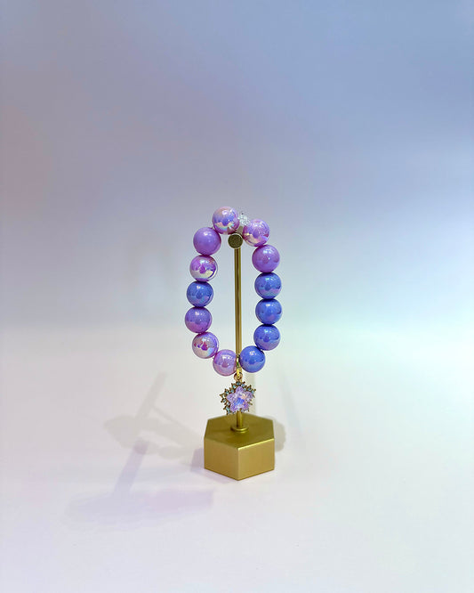 Purple beaded bracelet on a gold stand with a white background