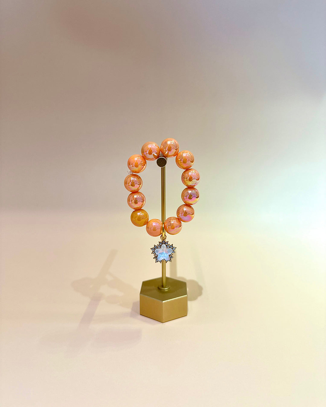 Peach-colored beaded bracelet on a gold stand with a star-shaped charm against a gradient background