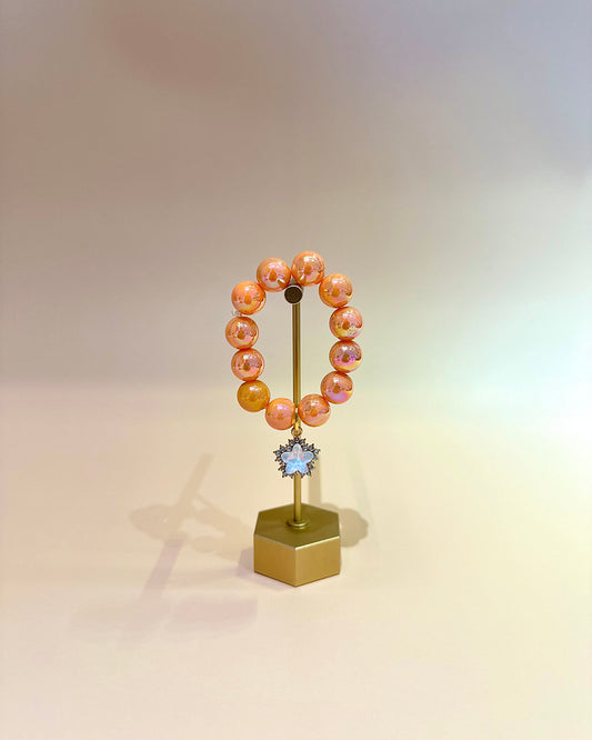 Peach-colored beaded bracelet on a gold stand with a star-shaped charm against a gradient background