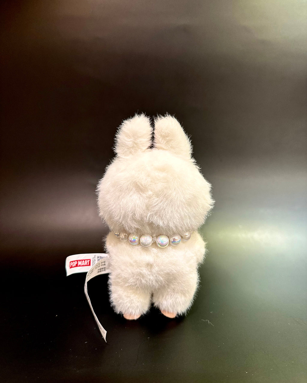 White plush toy with pearl necklace on a dark surface
