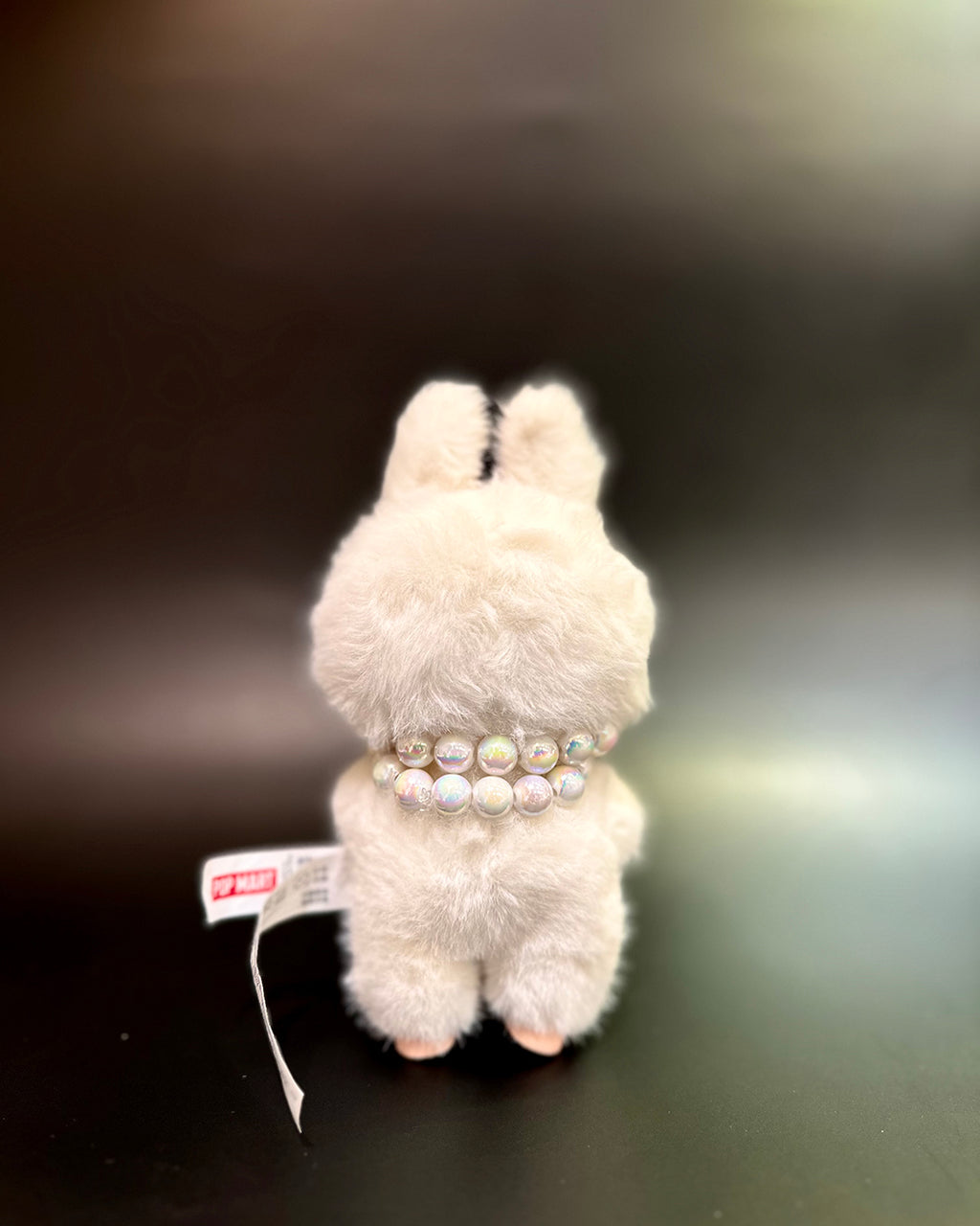 White plush toy with a pearl necklace on a dark background