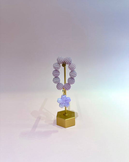 Decorative wreath with purple beads and a flower on a gold stand against a gradient background