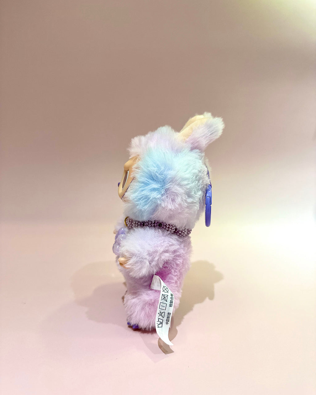 Multicolored plush toy with a tag on a beige background