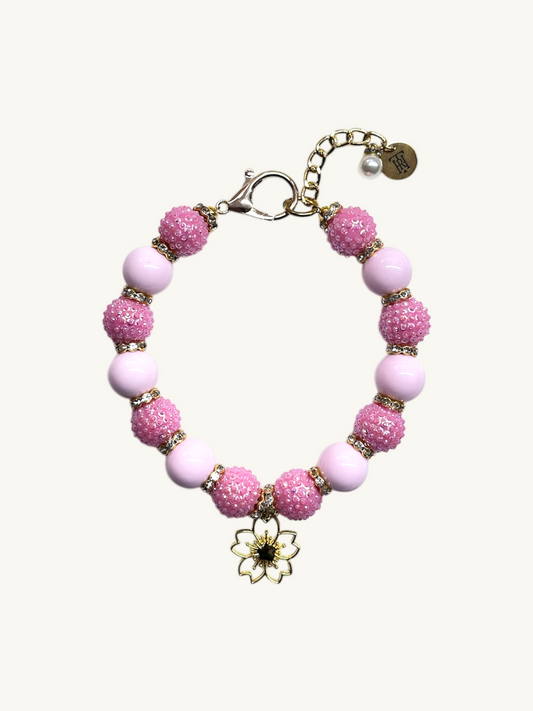 Pink beaded bracelet with a gold charm on a white background