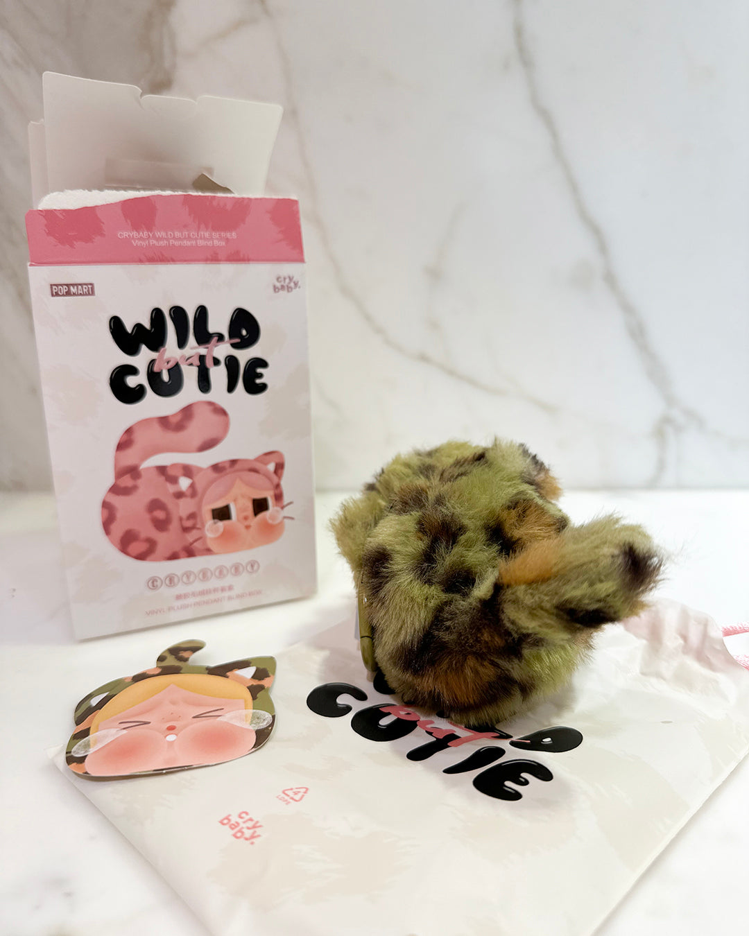 Small plush toy with packaging and branded items on a white background