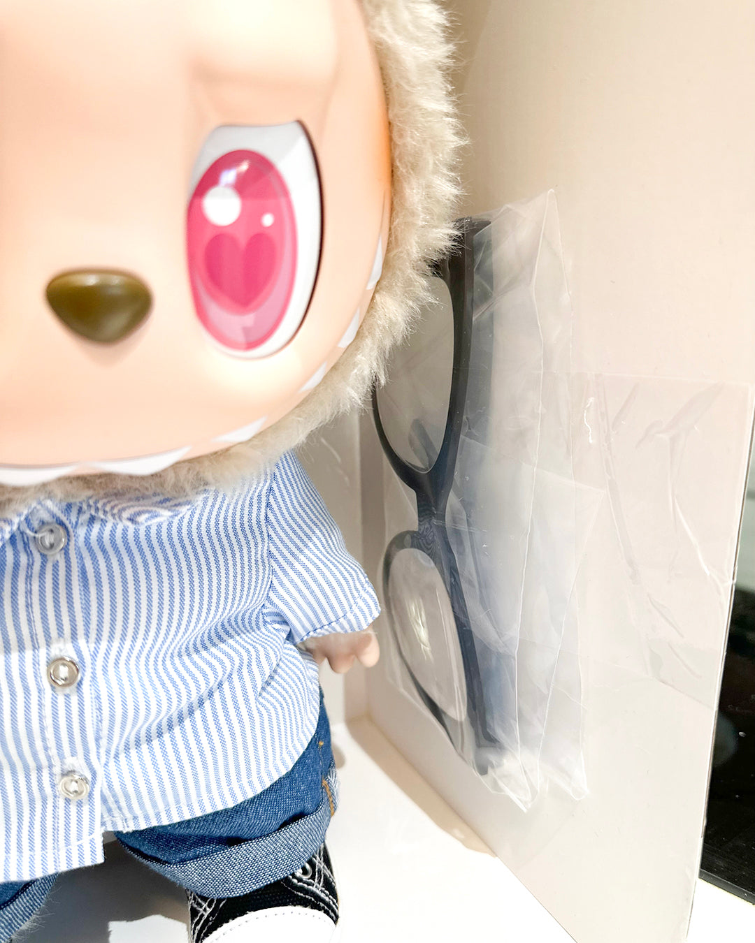 Close-up of a plush toy with large red eyes and a striped shirt, sitting on a white surface.