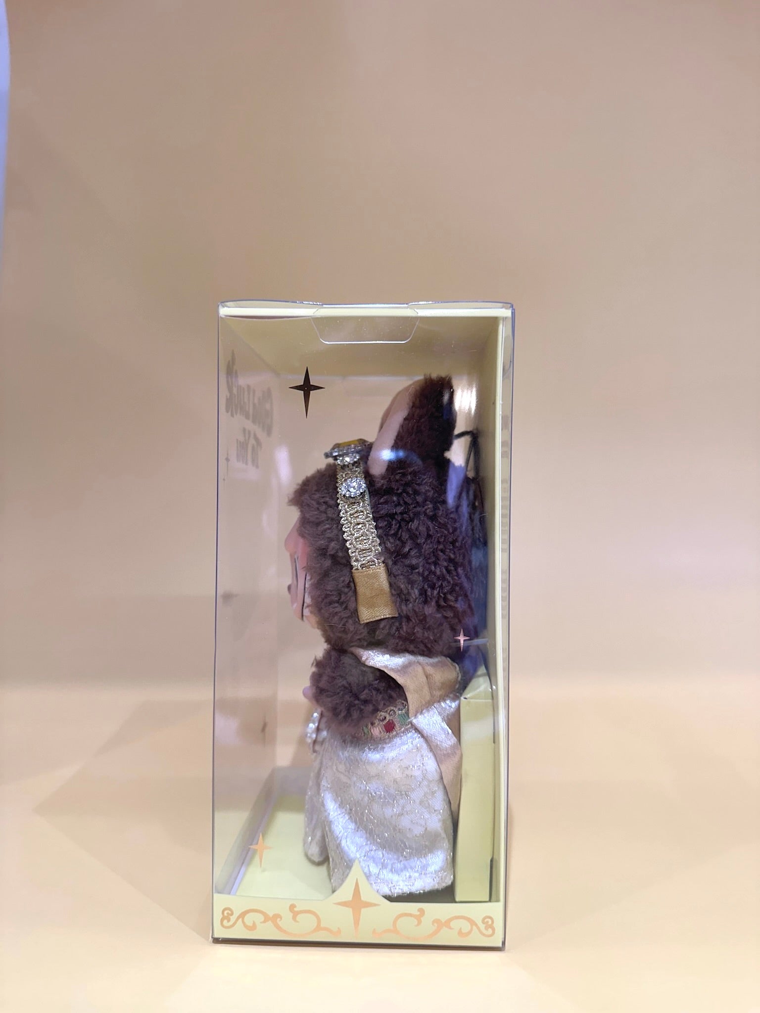 Barbie doll with curly hair and a tiara in a box on a beige background