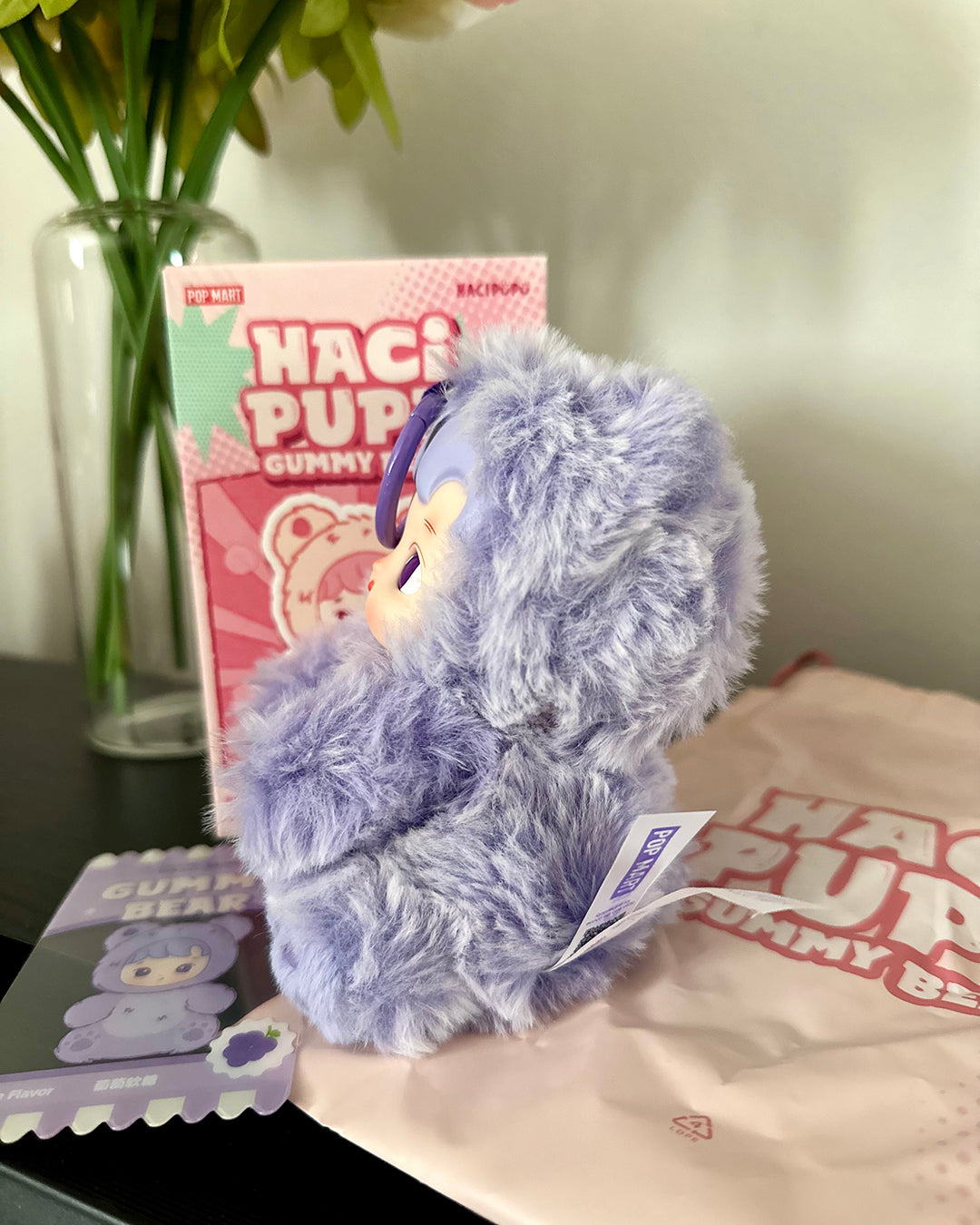 Plush toy with a tag on a surface next to a box and a vase.