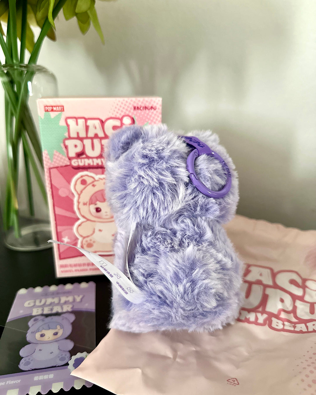 Purple fluffy toy with a ring on a surface with 'Haco Pup' packaging in the background.