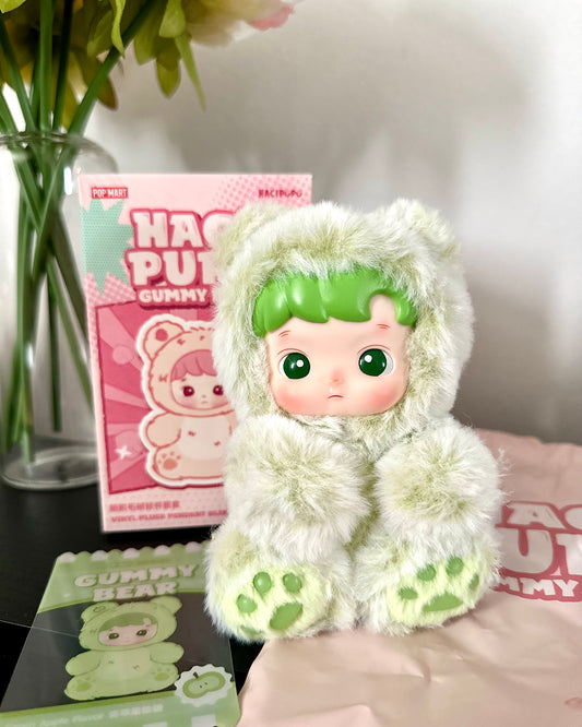 Plush toy with green hair and paws on a surface with packaging in the background