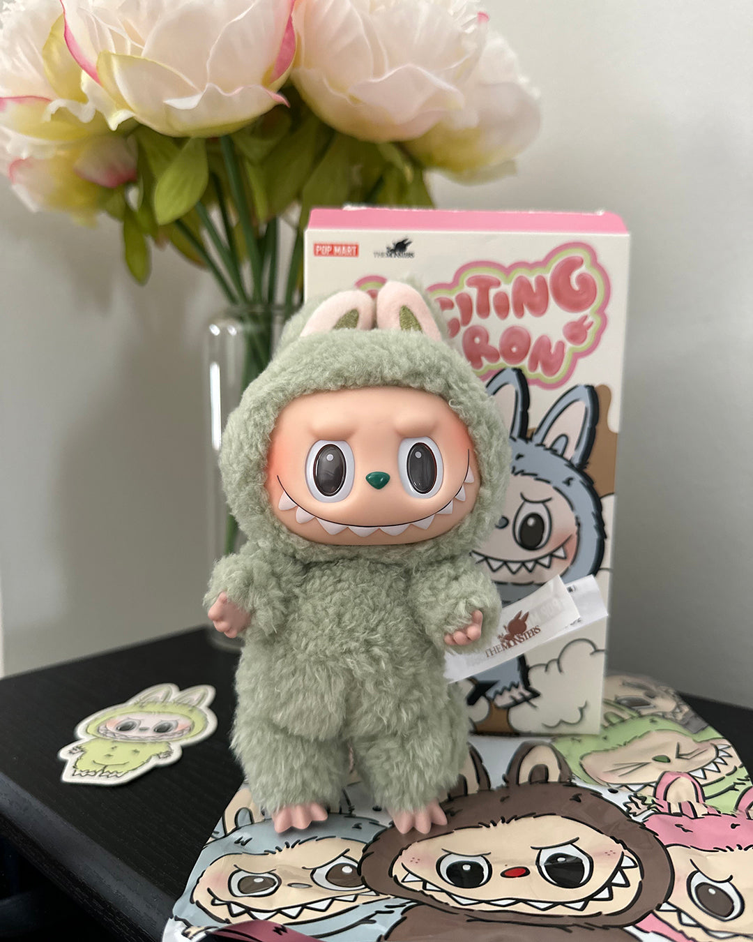 Plush toy in a green outfit with a box labeled 'Fighting Iron' and flowers in the background.