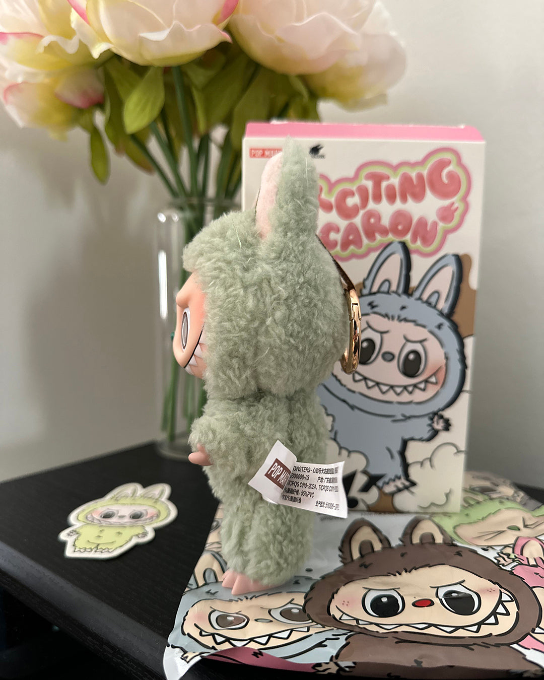 Green plush toy with cartoon character packaging and flowers in the background