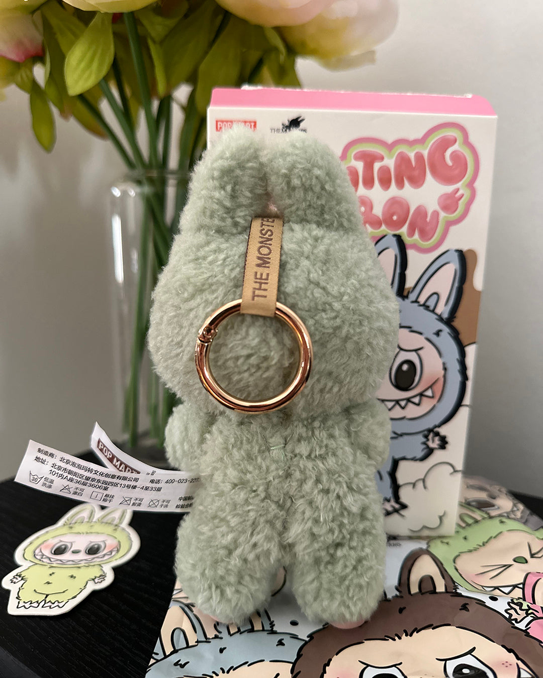 Green fluffy keychain with a rose gold ring on a colorful background with cartoon characters.