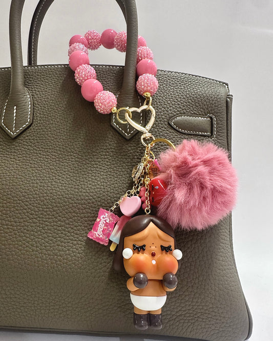 Pink beaded keychain with a character charm attached to a brown handbag.