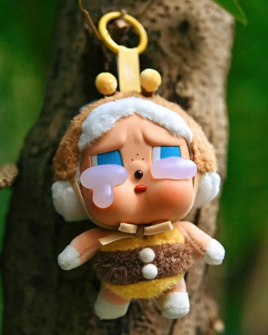 Plush toy character with blue eyes and a yellow hat hanging on a tree branch.