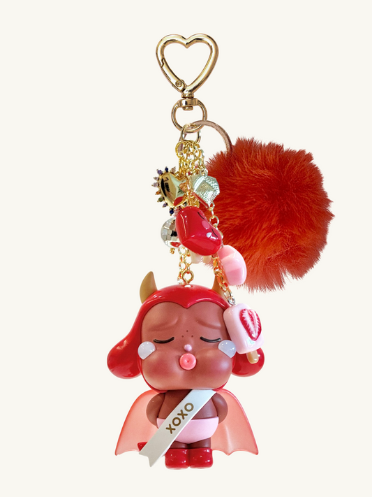 Keychain with cartoon character, heart-shaped keyring, and red pom-pom on a white background