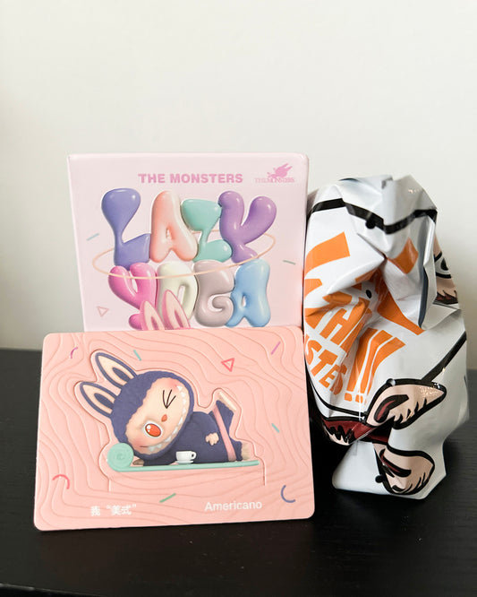Two decorative cards with cartoon designs and a ceramic monster figurine on a dark surface.