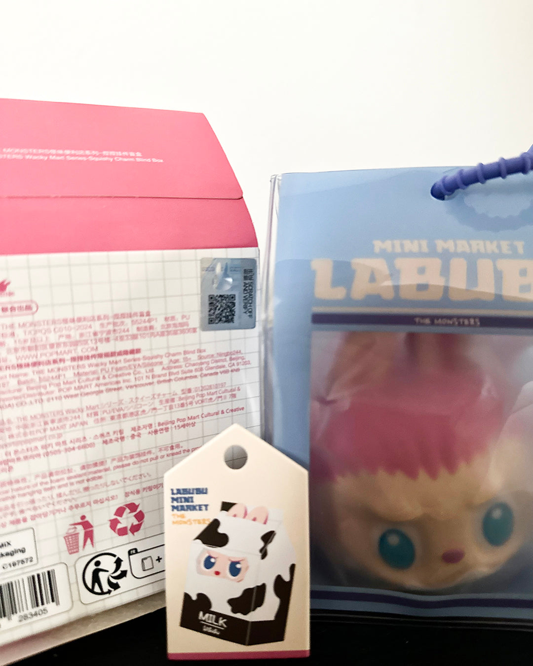 Product packaging with a pink box, blue bag, and a small toy figure on a white background