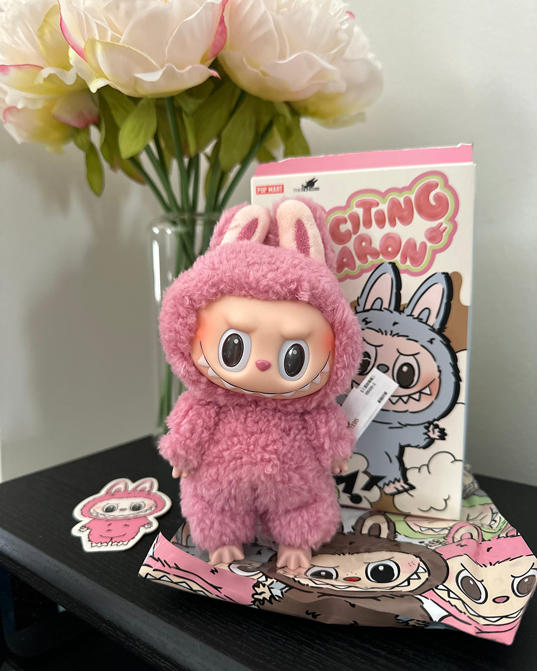 Plush toy in pink outfit with packaging and flowers in the background