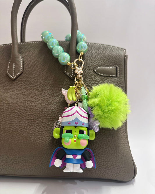 Colorful character keychain with a green pom-pom on a gray handbag.