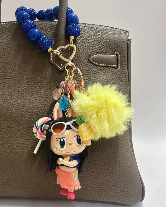 Colorful keychain with a character holding a pineapple attached to a gray handbag.