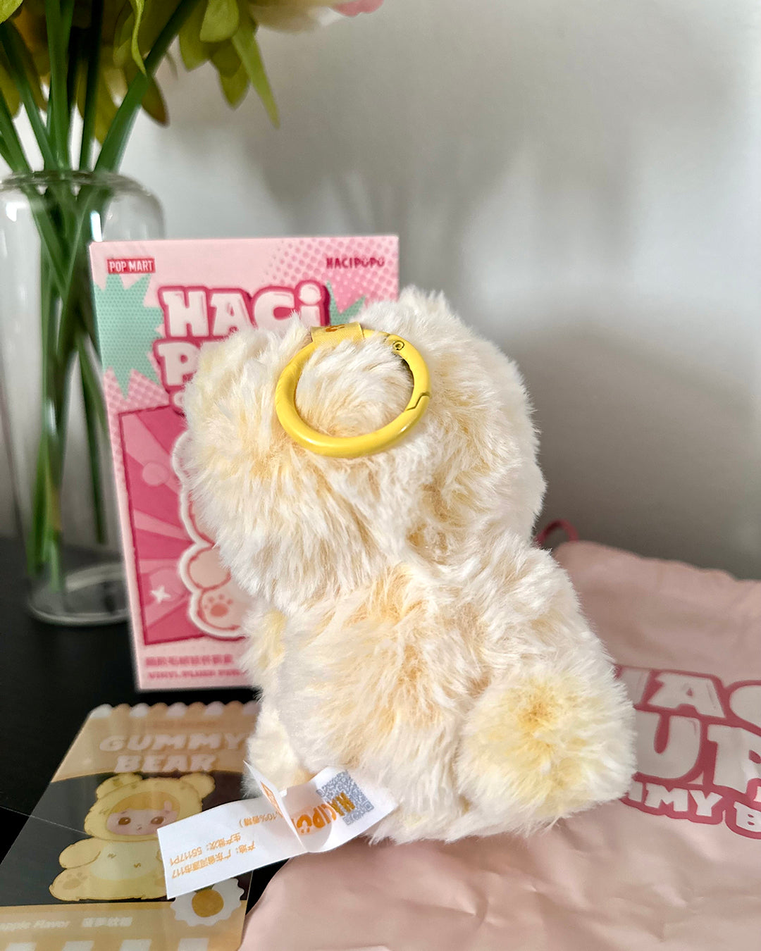 White plush toy with a yellow ring held by a person, with a pink box labeled 'HACI' in the background.